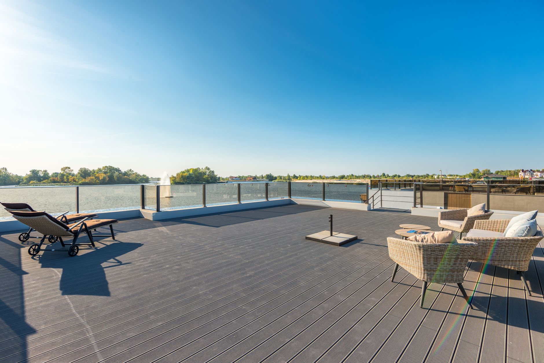 Spacious, sunny waterfront deck with modern wicker seating and lounge chairs overlooking a serene lake.