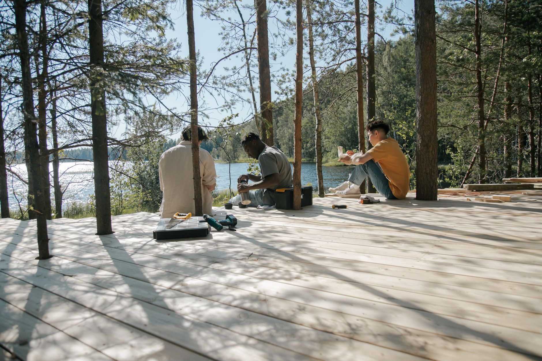 Group of workers enjoying a lunch break on a wooden deck in a serene forest setting.
