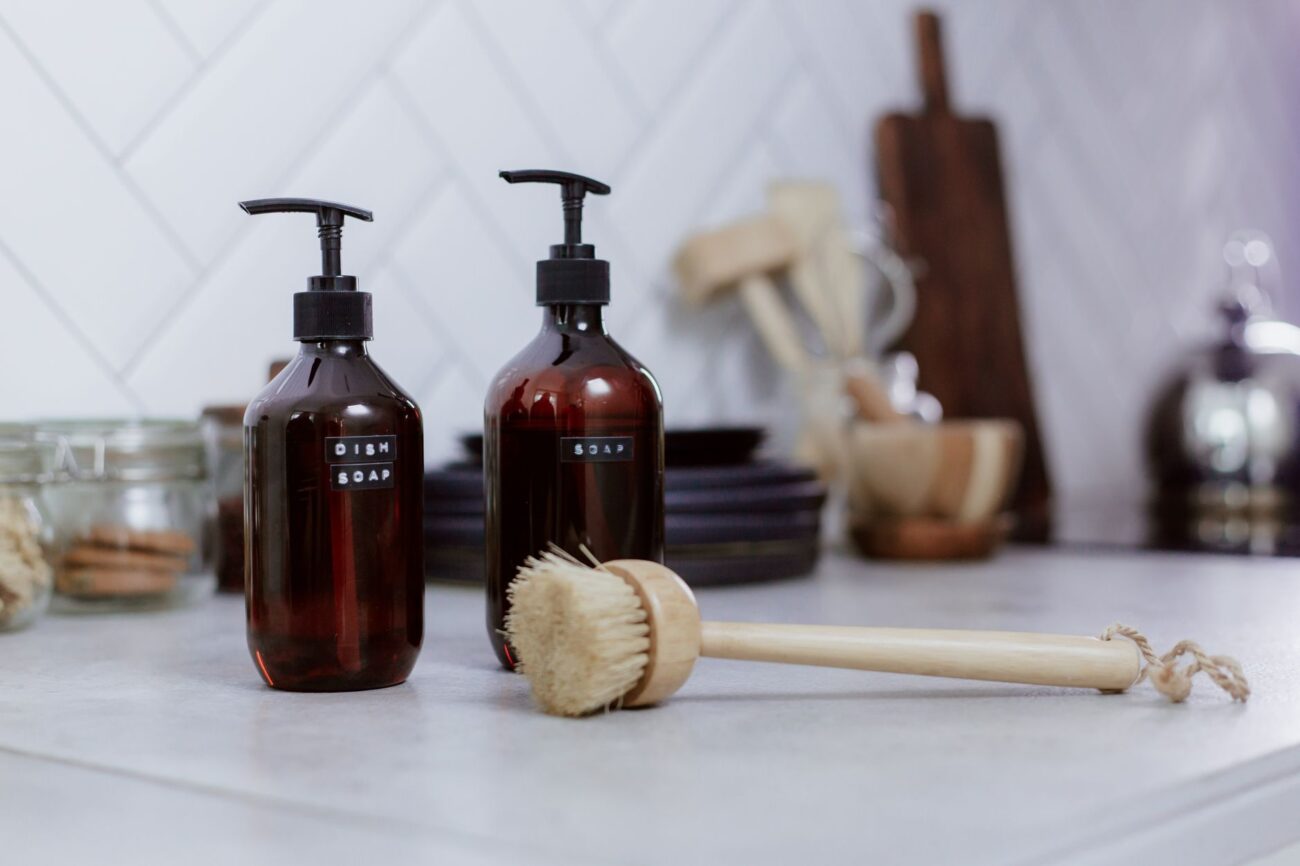 Aesthetic kitchen setting featuring amber soap bottles and dish brush for elegant cleaning. – Stop Over-Cleaning: 10 Household Items