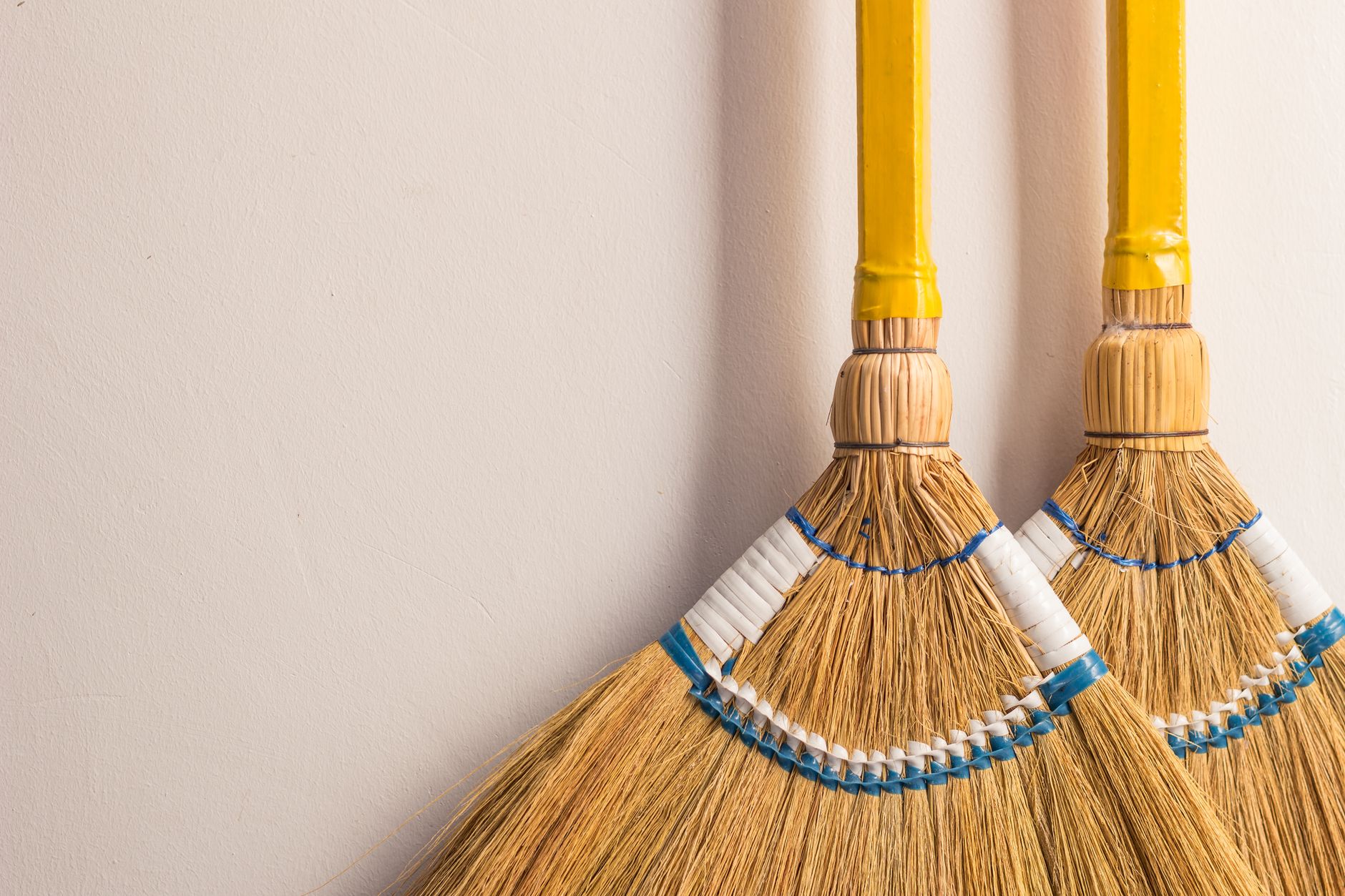 Pair of traditional Filipino walis tambo brooms on a neutral wall for home cleaning.