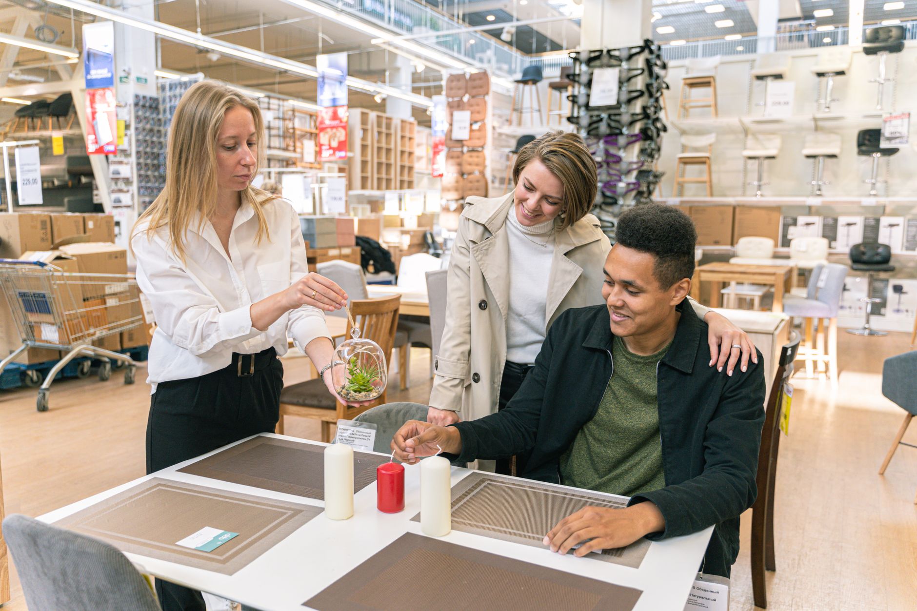 Three adults interacting in a furniture store, choosing decor items and smiling happily.