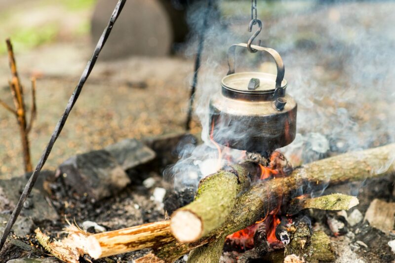 A traditional kettle hanging over a campfire, exuding a rustic outdoor cooking atmosphere. – cooking outside to beat the heat